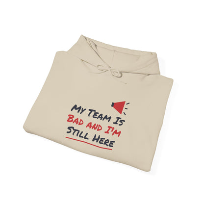 Light tan hoodie with front graphic text: “My Team Is Bad and I’m Still Here”