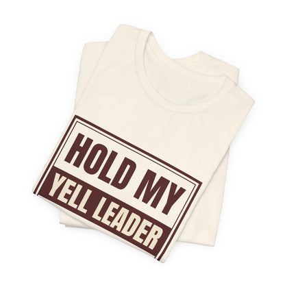 Natural crewneck tee folded; close-up of "HOLD MY YELL LEADER" graphic